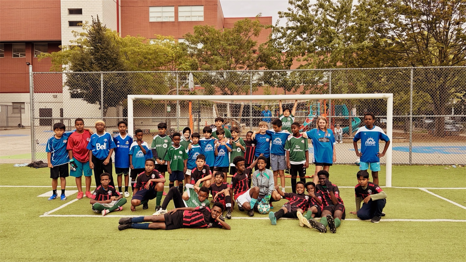 Young soccer players gathered together in front of a goal on an outdoor pitch.